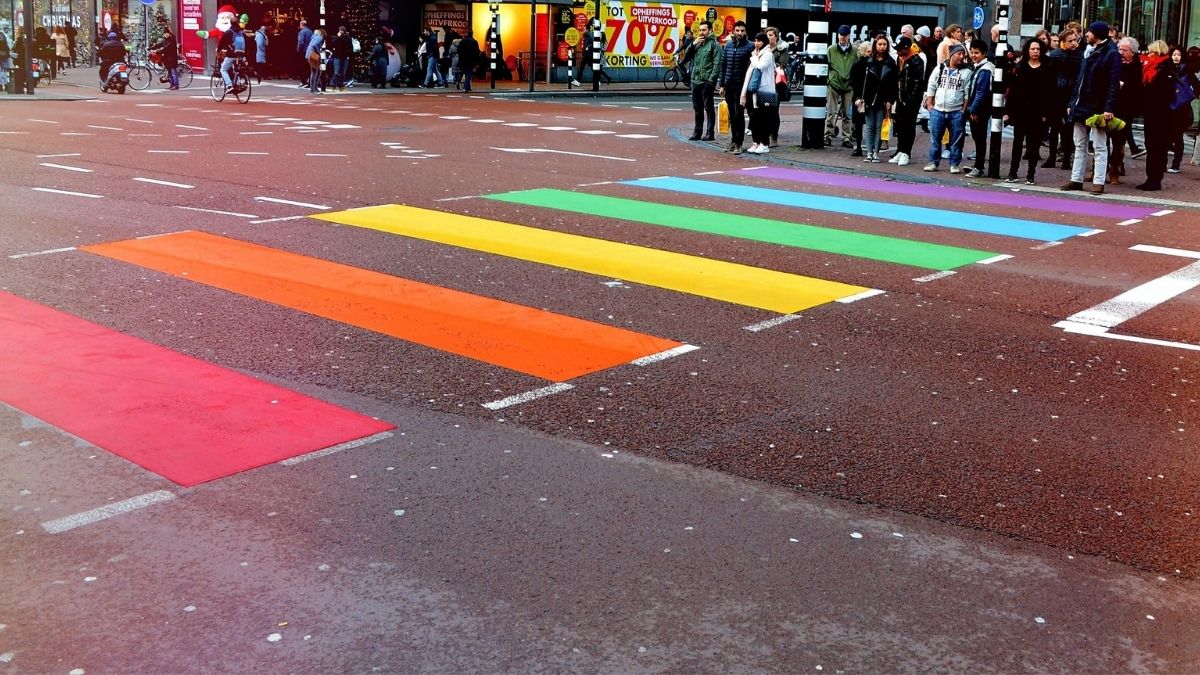 Nell'immagine si vedono delle strisce pedonali colorate con i colori dell'arcobaleno e molte persone.
