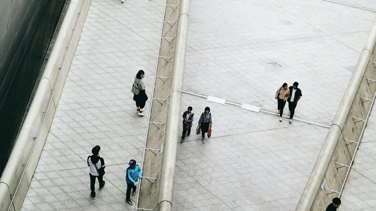 Ci sono persone che camminano in uno spiazzo, diviso da muri, con corrimano e completamente accessibile e senza scale.