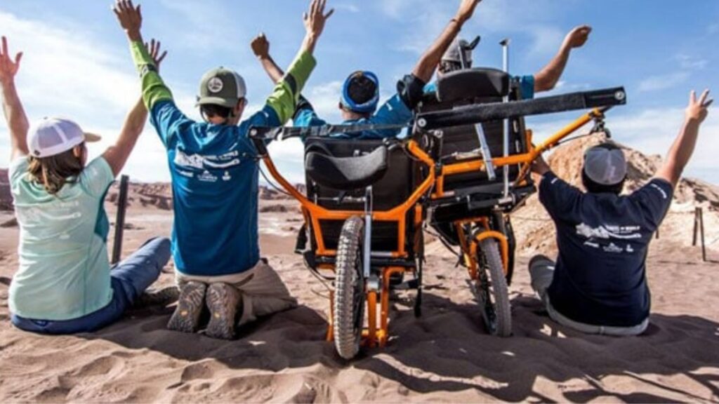 un gruppo di persone sulla spiaggia, due di loro in carrozzina.