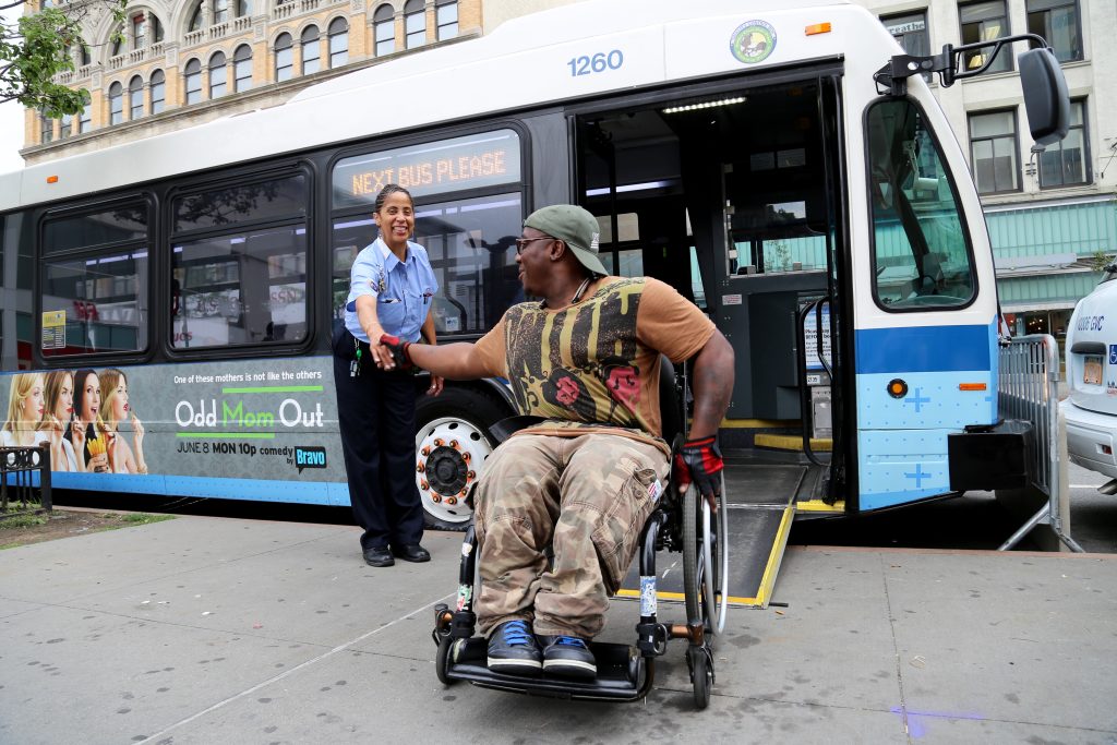 Ragazzo in carrozzina che stringe la mano a un addetto mentre scende da un bus accessibile