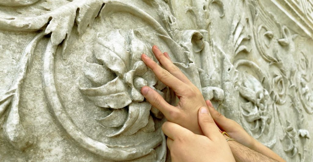 Una mano tocca un dettaglio durante il percorso tattile all'Ara Pacis a Roma
