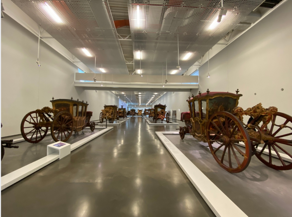 Museo Nazionale delle Carrozze Lisbona: una panoramica del museo, in cui si vede un lungo corridoio con diverse carrozze marroni sui lati.