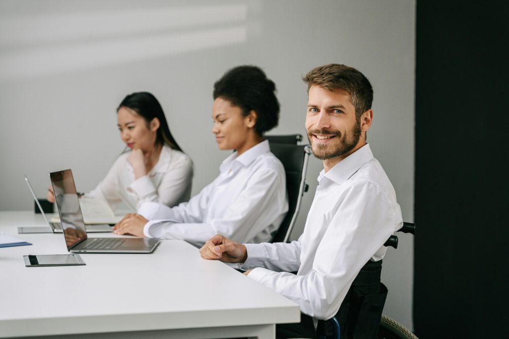 Azienda inclusiva. Persone in ufficio, di cui una in carrozzina. Posizionate in ufficio, alla scrivania, metre lavorano.